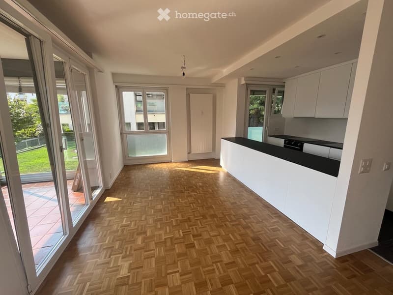 Modern kitchen with white cabinets, a black countertop, and herringbone wooden flooring. Large windows and sliding glass doors lead to a garden area.