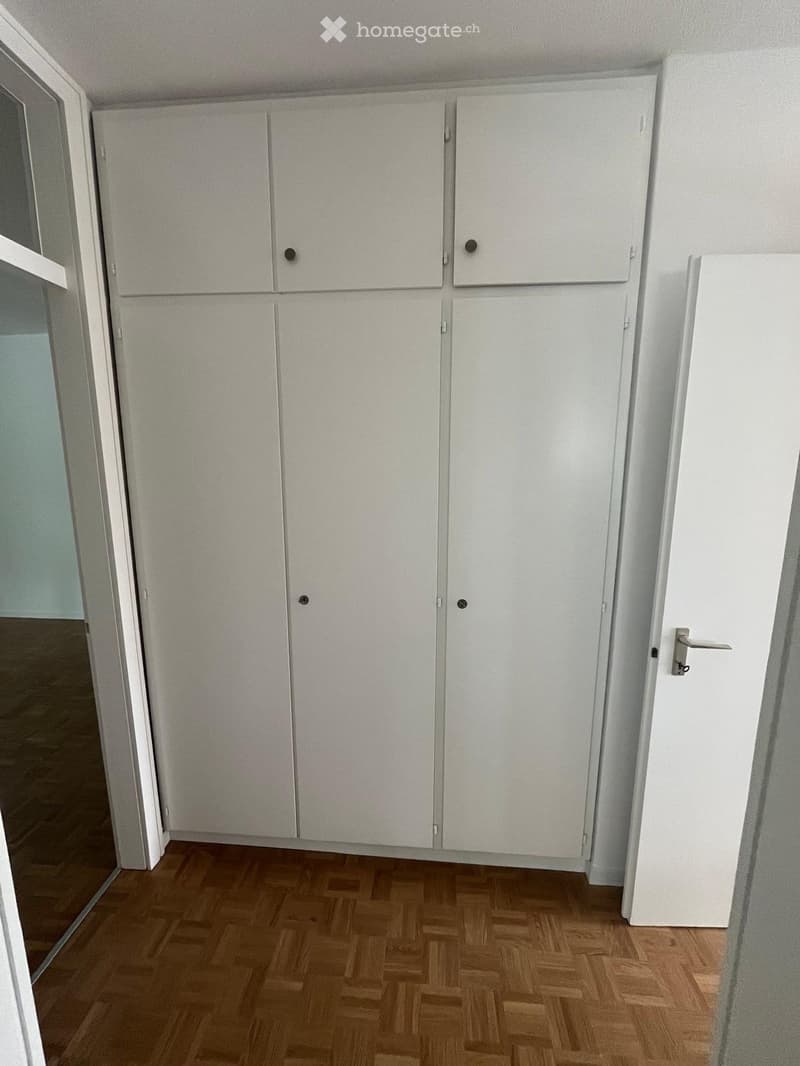 Empty room with white cabinets and wooden flooring.