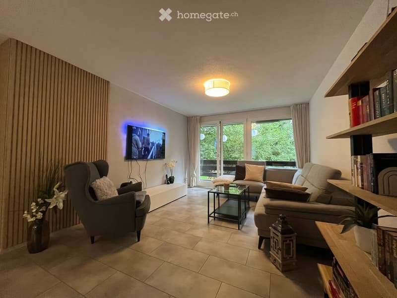 Modern living room with a grey sectional sofa, armchair, coffee table, television, bookshelf, and decorative vases.
