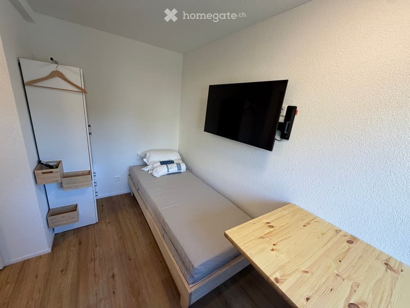 Small room with single bed, TV on wall, wooden table, wooden floor, closet
