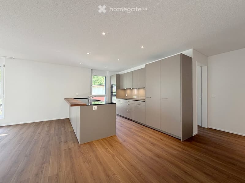 Modern kitchen with light grey cabinets, a central island with a dark countertop, and wooden flooring.