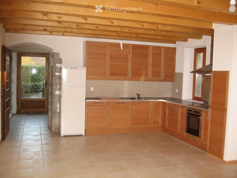 Bright kitchen with wooden cabinets, tiled floor, and white appliances including a refrigerator, sink, and oven.