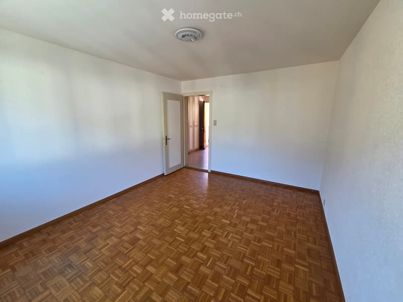 Empty room with light-colored walls and wooden parquet flooring, featuring a single door leading to another room.