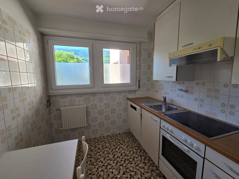 The kitchen features a tiled backsplash, wooden countertops, a sink, stove, oven, and cabinets. There is a window with a view of greenery outside.