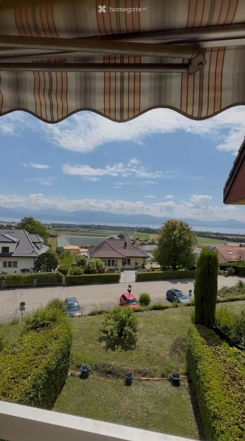 Balcony with striped awning, overlooking a landscaped garden, parking area, and distant mountains.