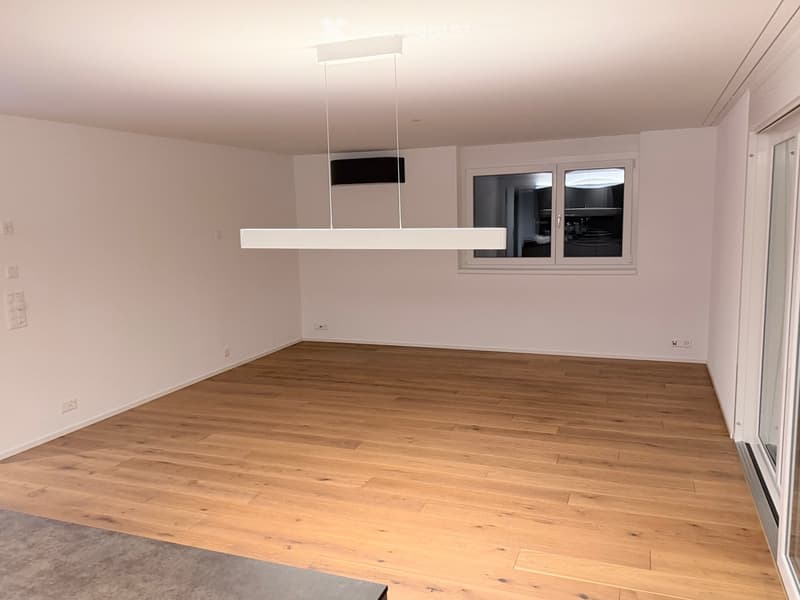 Empty room with light pink walls, wooden flooring, and large windows. No furniture or equipment present.