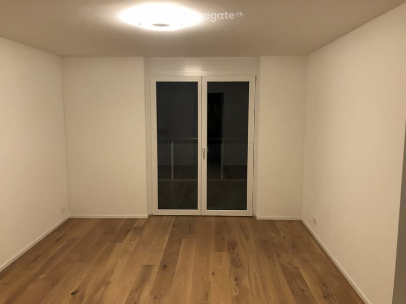 Empty room with wooden flooring, white walls, and a large glass door leading outside.