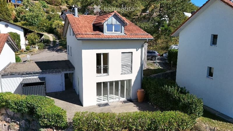 Two-story house with white exterior, red-tiled roof, garage, and parking area.