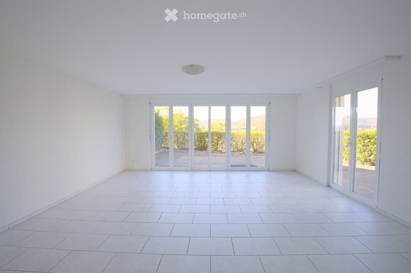Empty room with white tiled flooring, white walls, and large glass sliding doors leading to an outdoor area.