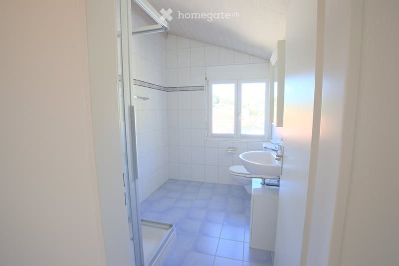 Modern bathroom with white tiles, a bathtub, toilet, sink, and a window offering a view.