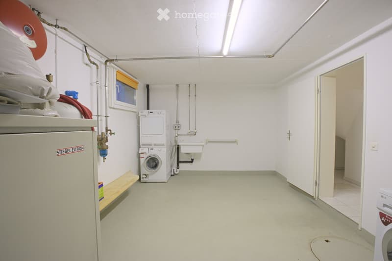 Utility room with white walls, a washing machine, a dishwasher, a sink, and a small wooden bench.