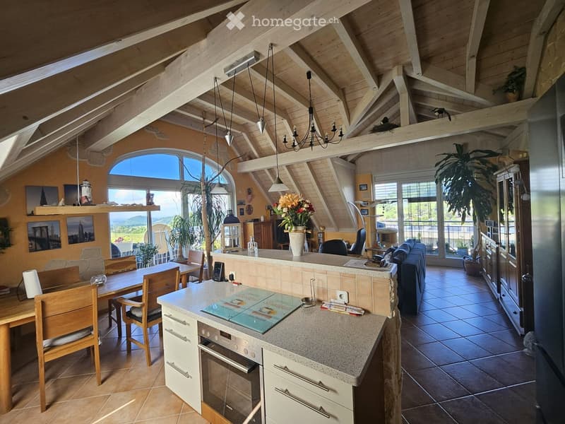 Open-plan living and dining area with exposed wooden beams, large windows, a kitchen island, dining table, sofa, and pendant lights.