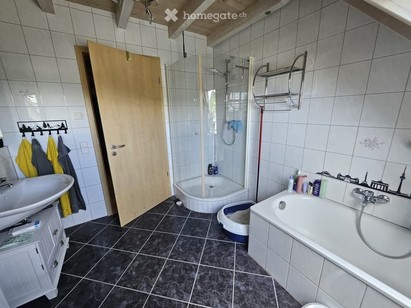 Bathroom with a sink, bathtub, shower, and a cat litter box. Features a wooden door, towel rack, and various toiletries on the edge of the bathtub.