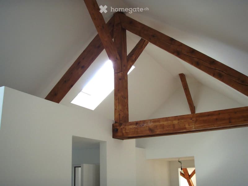 A modern hallway with exposed wooden beams and a skylight, featuring white walls and a clean, minimalist design.