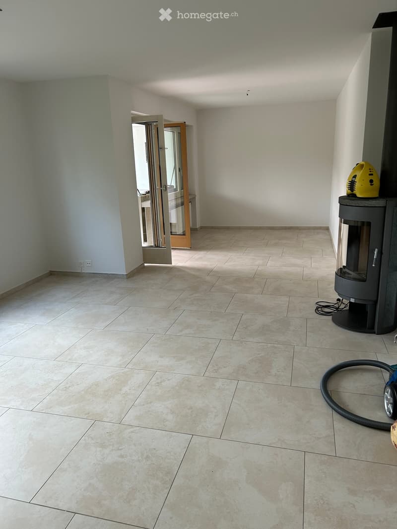 Empty room with tiled floor and white walls, featuring a fireplace and a vacuum cleaner in the corner.