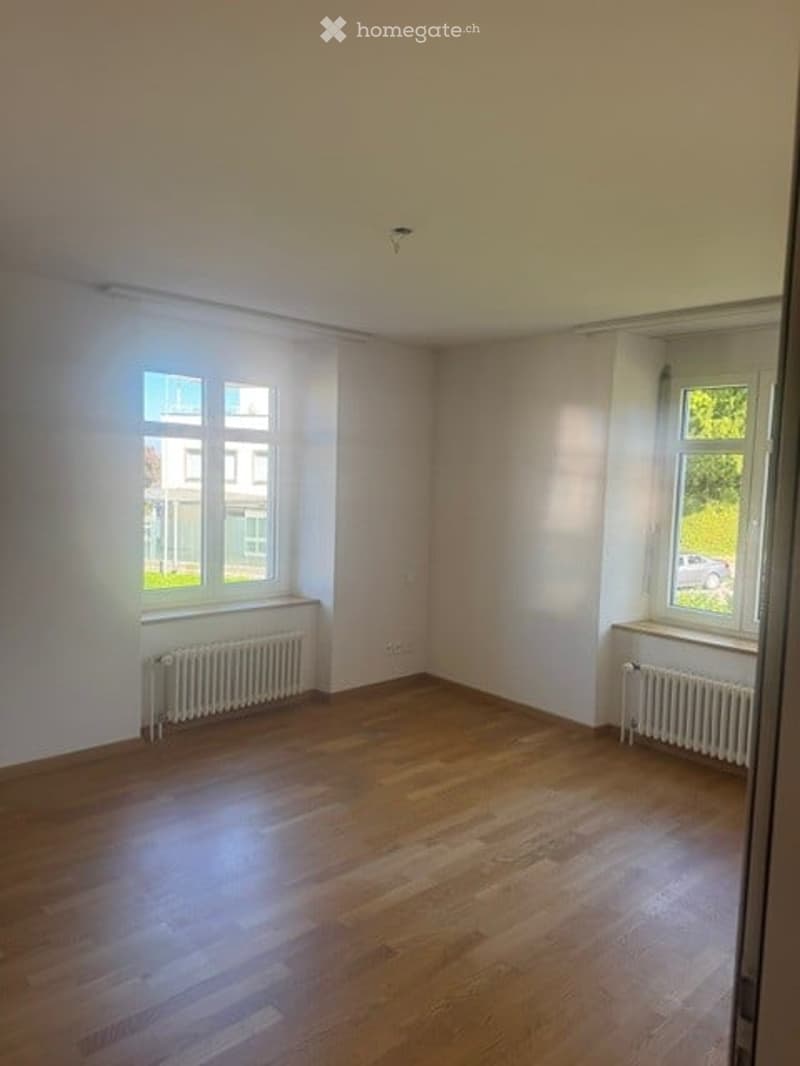 Empty room with wooden flooring, white walls, and large windows with radiators underneath. No furniture or equipment present.