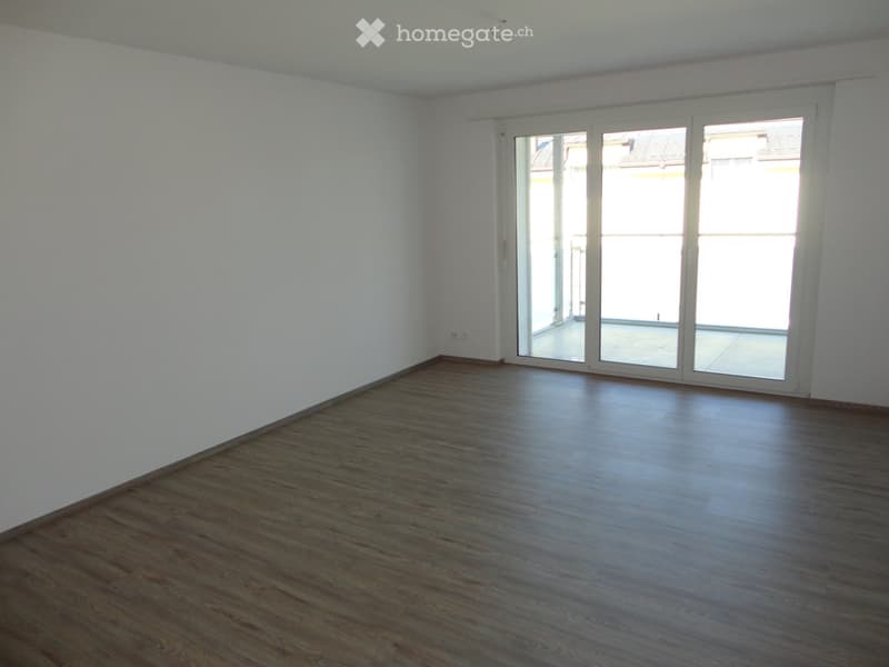 Empty room with wooden flooring and white walls, featuring large glass sliding doors leading to a balcony.