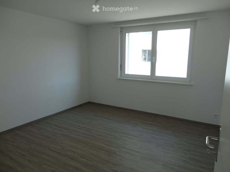 Empty room with wooden flooring, white walls, and a large window with blinds.