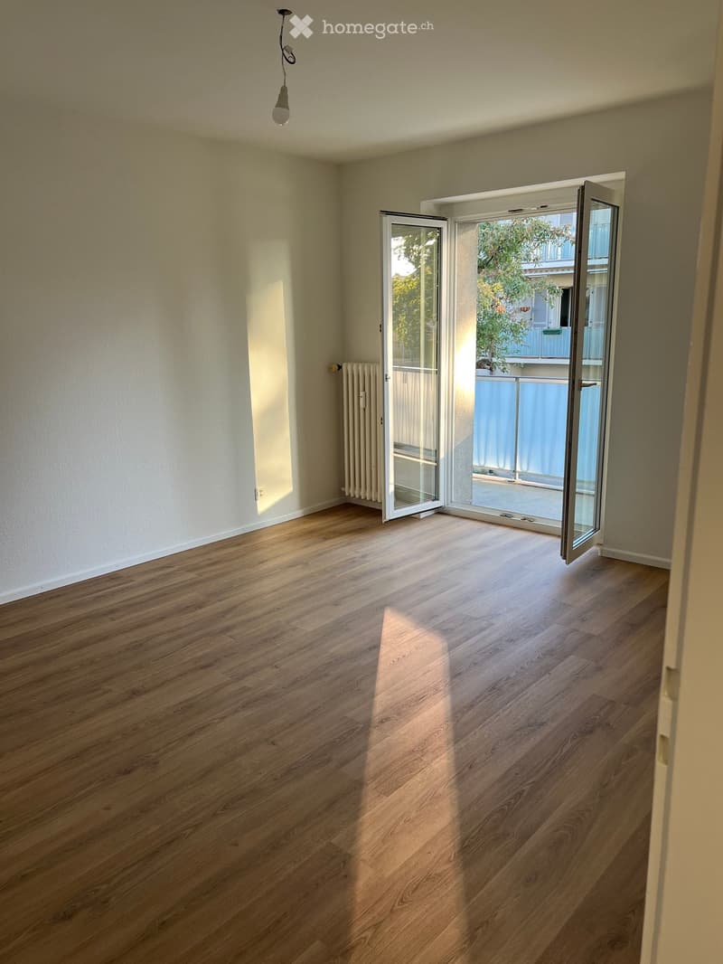 Empty room with wooden flooring, white walls, and large sliding glass doors leading to a balcony area.