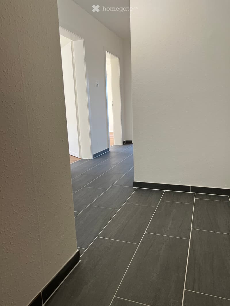 Empty hallway with dark grey tiled floor and white walls, featuring two open doors leading to other rooms.