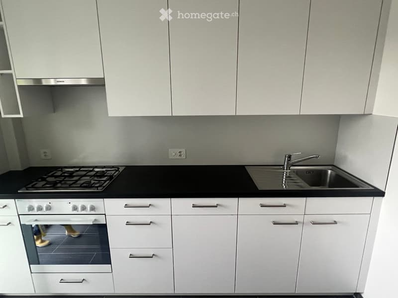 Modern kitchen with white cabinets, black countertops, a gas stove, an oven, and a stainless steel sink with a faucet.