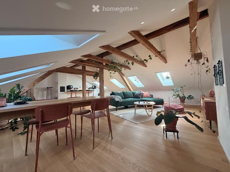Open-concept living and dining area with wooden beams, skylights, and modern furniture including a green sofa, coffee table, dining table, and chairs.