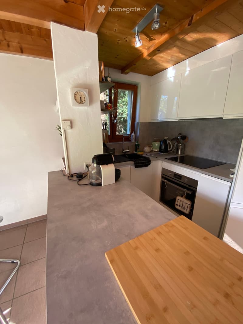 Modern kitchen with white cabinets, grey countertops, and a wooden island. Features an oven, coffee maker, and a clock on the wall.