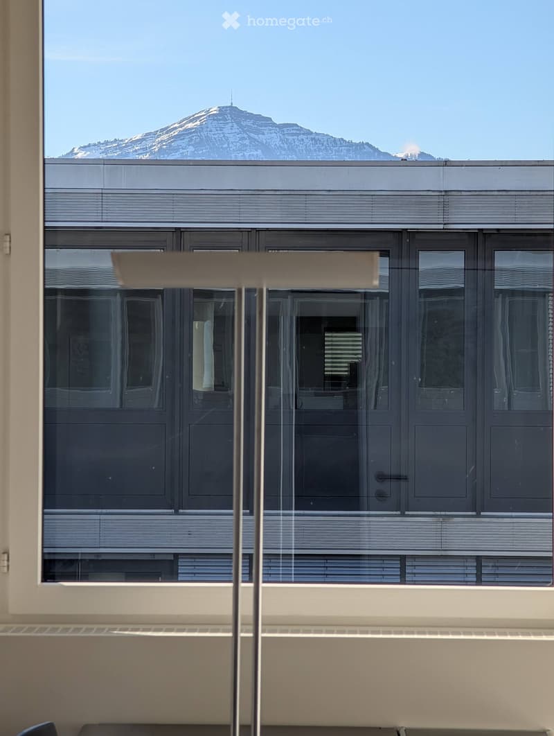 View from a room showing a modern building exterior with large windows and a scenic mountain view outside.