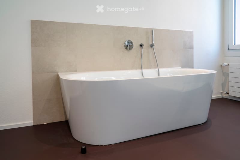 Modern bathroom with a large, freestanding white bathtub, sleek faucet fixtures, and a dark brown floor.