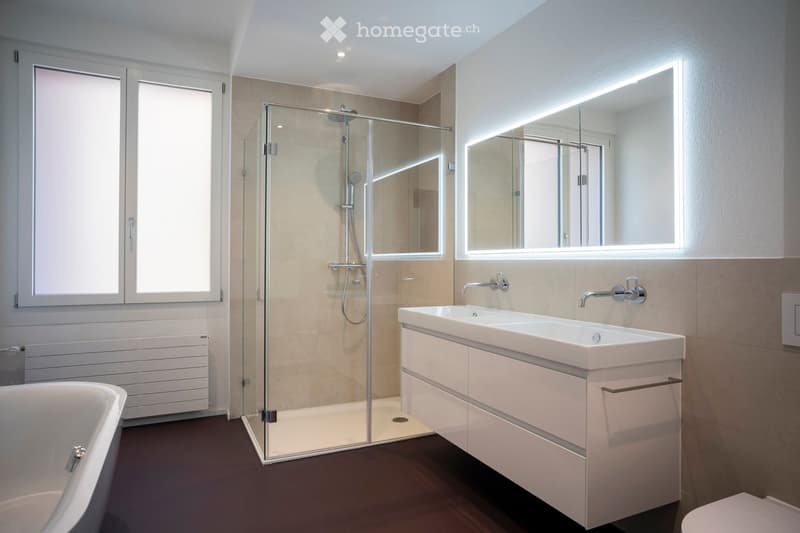 Modern bathroom with a bathtub, glass-enclosed shower, double sink with modern faucet, illuminated mirror, and a radiator.