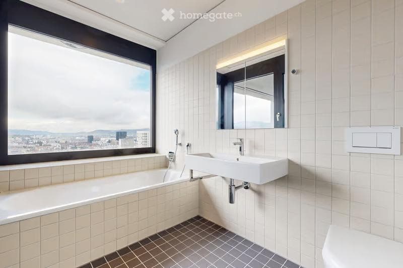 Modern bathroom with a large window offering a city view, featuring a bathtub, a sink, and a mirror with built-in lighting.