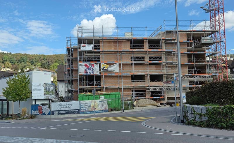 Multi-story building under construction with scaffolding, exposed brickwork, and banners on the facade. The building is partially completed with visible windows and structural supports.