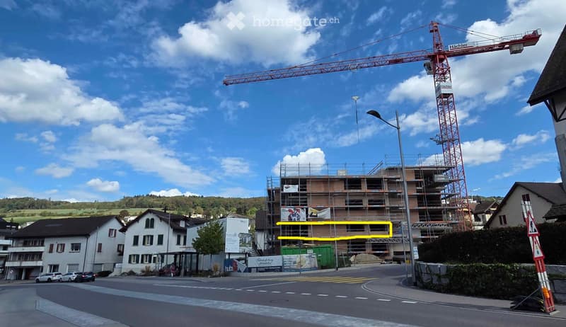A multi-story building under construction with scaffolding, a large red crane, and surrounding residential houses.