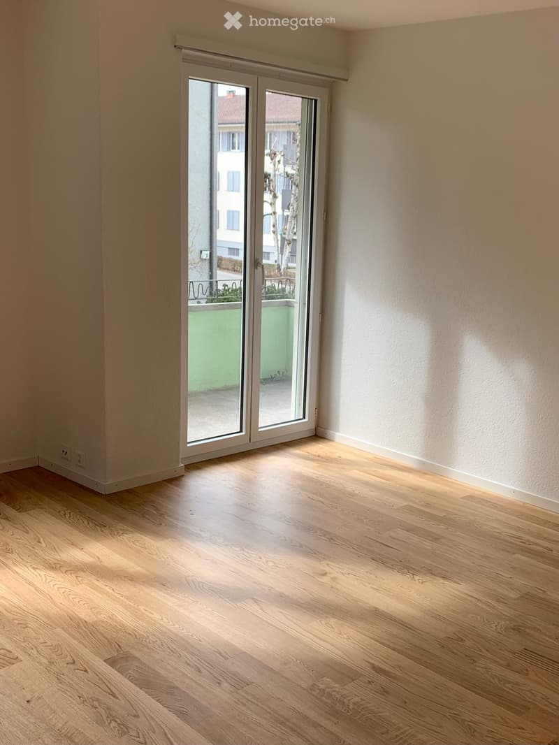 Empty room with light wooden flooring and large sliding glass doors leading to a balcony area.