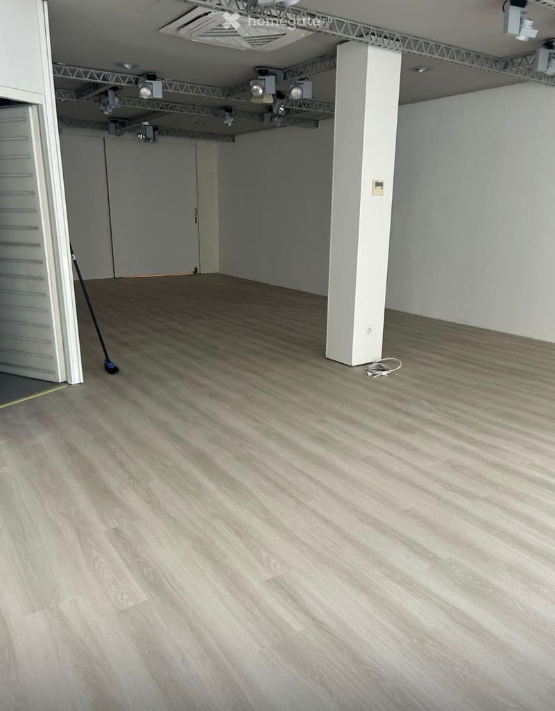Empty room with wooden flooring, white walls, and a single door visible on the left side.