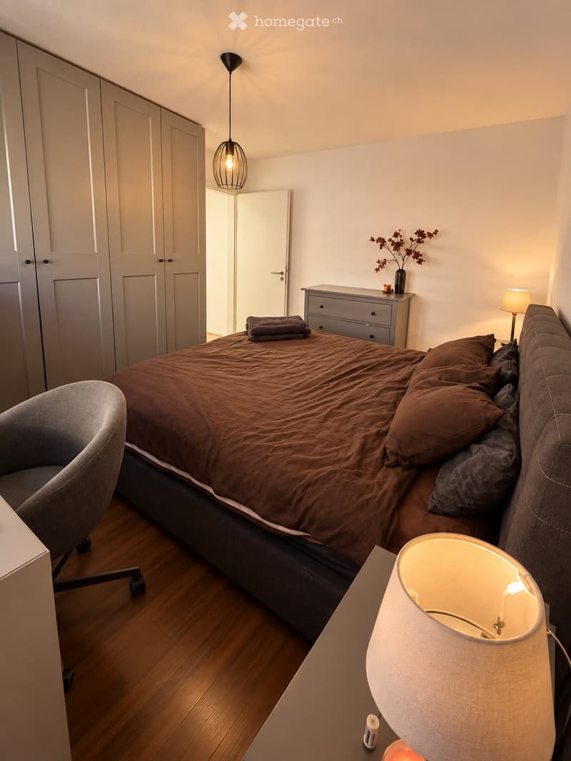 Cozy bedroom with a large bed, nightstand, chair, and decorative items.
