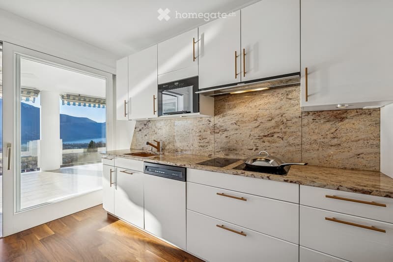 Modern kitchen with granite countertops, white cabinets, gas stove, sink, microwave, dishwasher, wooden floor, balcony view