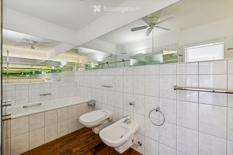 modern bathroom with white tiles, bathtub, toilet, bidet, double ceiling fans, glass wall, glass door