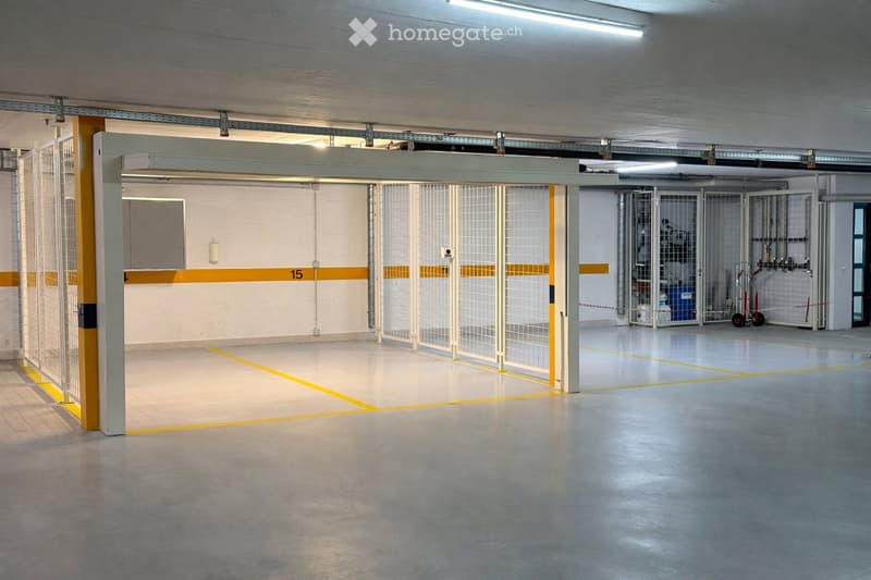 Empty underground parking area with marked parking spaces, metal barriers, and a gated section.