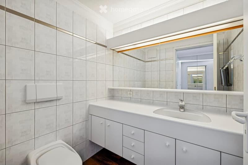 Bathroom with white tiled walls, white floor, white cabinet, white sink, faucet, white toilet