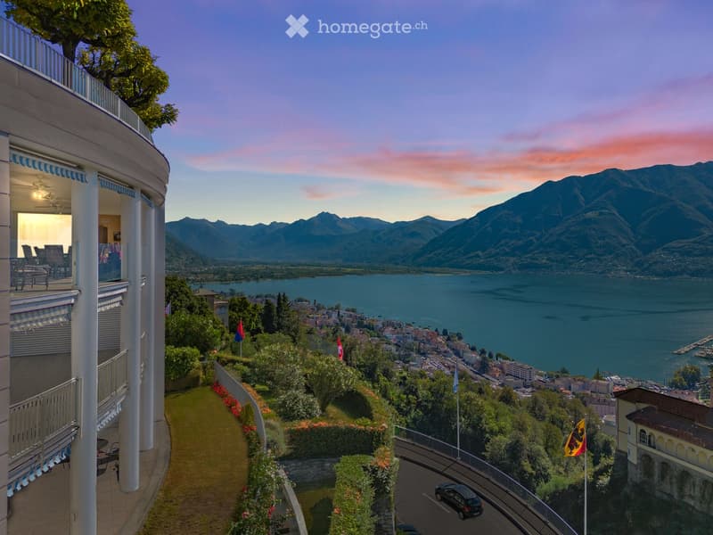 building with a balcony, overlooking a lake and mountains, with surrounding vegetation