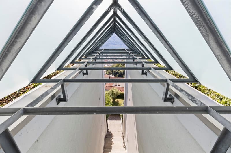 a triangular exterior space with large windows and an internal staircase, with an upper level garden area