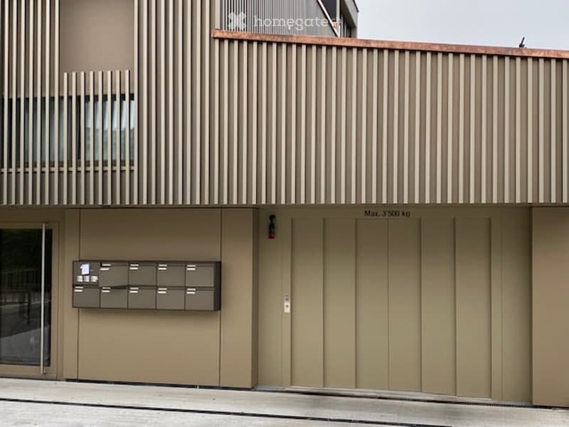 Modern building with a garage, metal panels, glass door, mailboxes, and a sign indicating a weight limit.