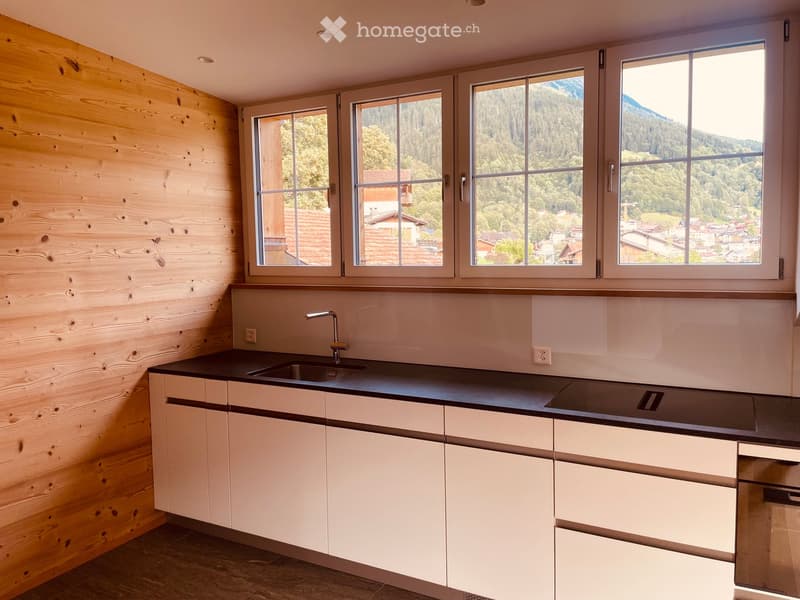 Modern kitchen with white cabinets, black countertops, and a stainless steel sink. Large windows offer a scenic mountain view.