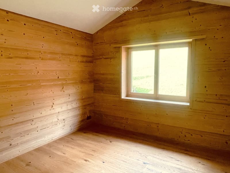 Empty room with wooden walls and floor, featuring a single window allowing natural light to enter.