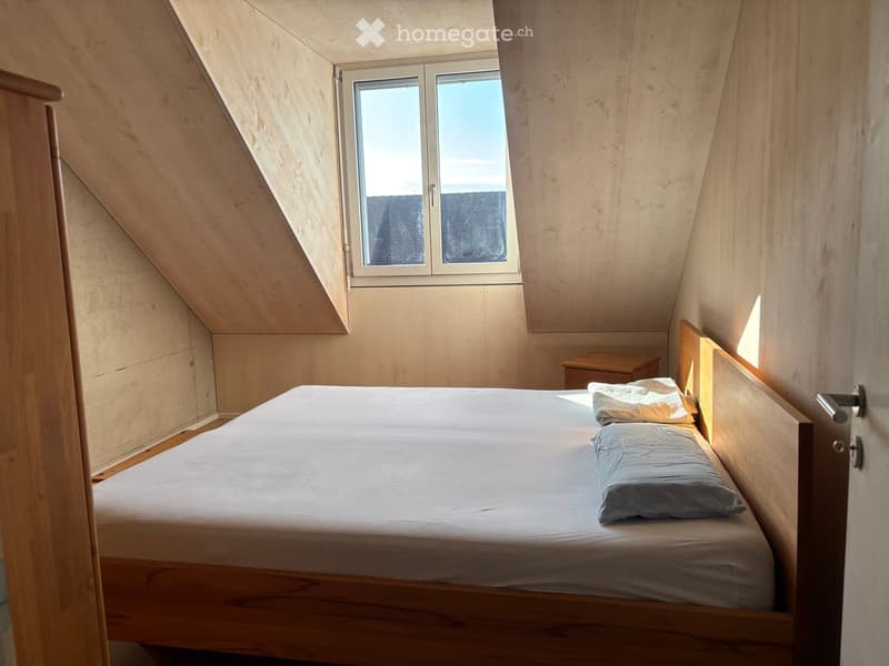 Cozy attic bedroom with wooden walls, slanted ceiling, and a single bed with light bedding and pillows.