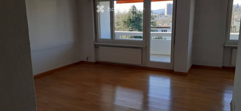 Empty room with wooden flooring, large windows, and a balcony access door.