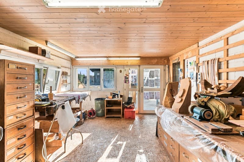 A spacious workshop with wooden walls and ceiling, large windows, and various woodworking tools and equipment.