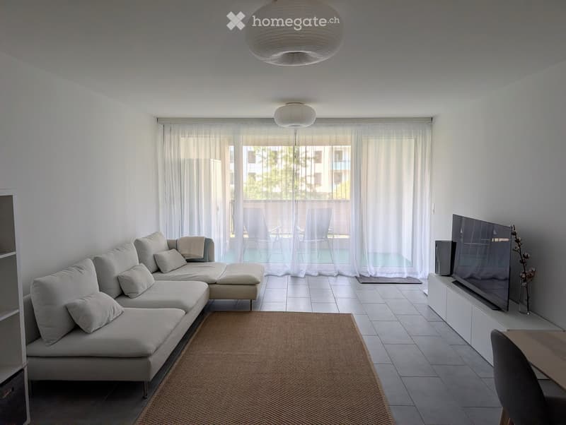 Modern living room with a white sofa, coffee table, TV, and a view of a balcony area with outdoor furniture.