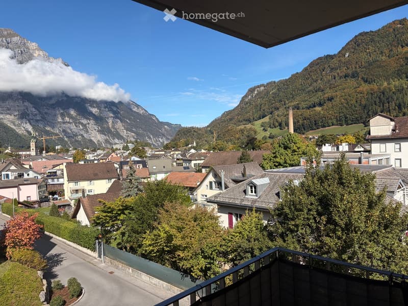 Balcony overlooking a town with houses, trees, and mountains in the background.